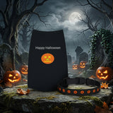 A black Halloween-themed pet collar with orange jack-o'-lantern face details and a matching black pouch printed with 'Happy Halloween' and an orange pumpkin graphic, displayed in a spooky graveyard scene with pumpkins and a full moon.